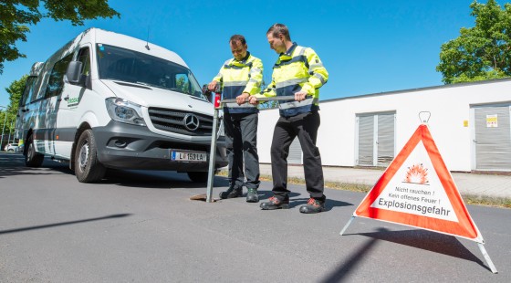 Zwei Mitarbeiter führen eine Schieberkontrolle durch, im Hintergrund ist ein Dienstwagen, im Vordergrund ein Warndreieck zu sehen.