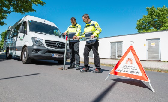 Zwei Mitarbeiter führen eine Schieberkontrolle durch, im Hintergrund ist ein Dienstwagen, im Vordergrund ein Warndreieck zu sehen.