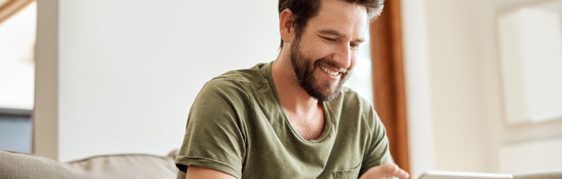 Ein Mann sitzt auf der Couch und bedient ein Tablet.