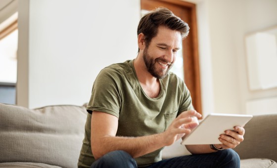 Ein Mann sitzt auf der Couch und bedient ein Tablet.