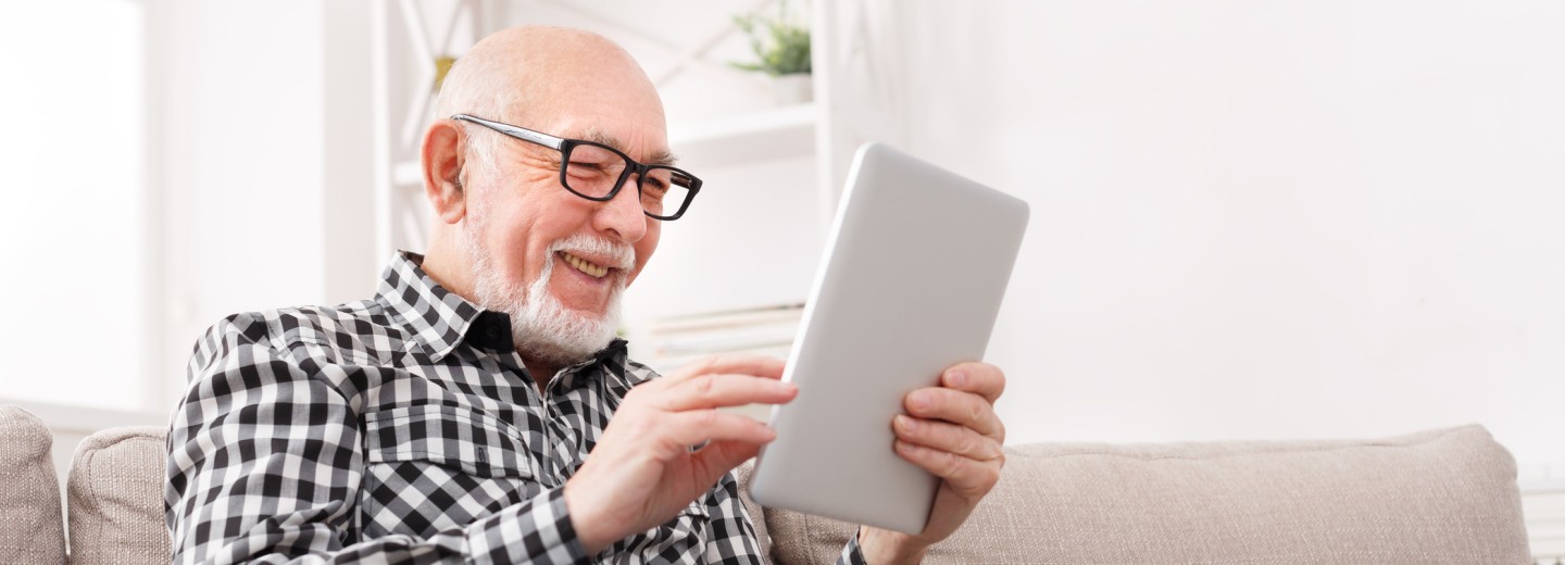 Ein älterer Herr sitzt auf der Couch und bedient sein Tablet.